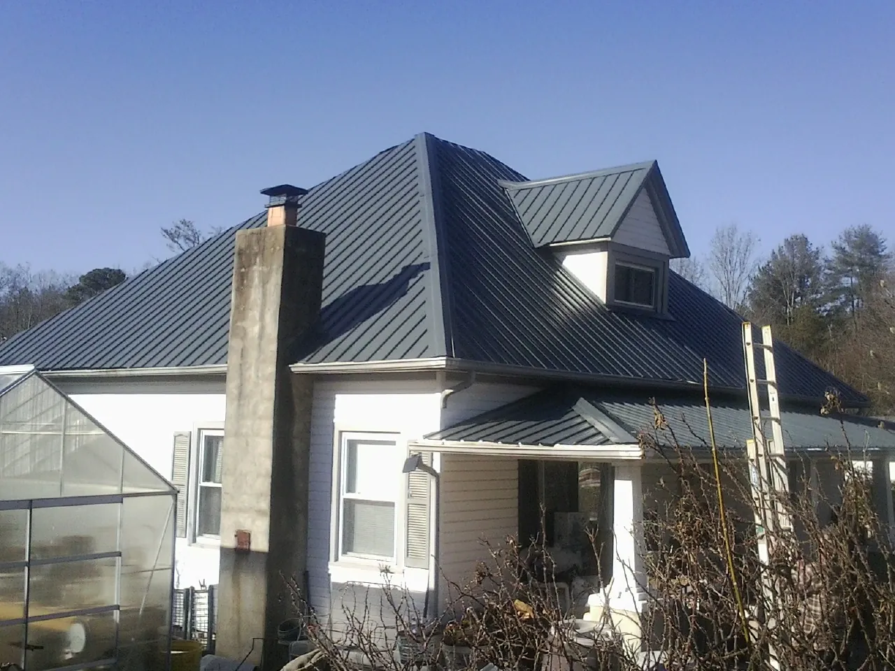 Dark blue standing seam metal roof on a white farmhouse with dormer — Slate & Tile Roof Repair by Roofing Brothers in Overpeck