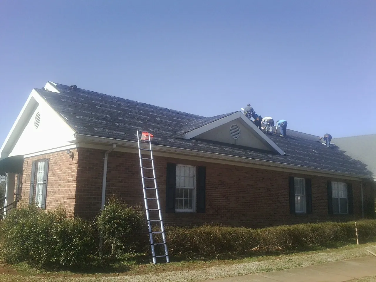 Crew tearing shingles off a brick ranch roof with a ladder set — Emergency Roof Repair work by our crew in Overpeck