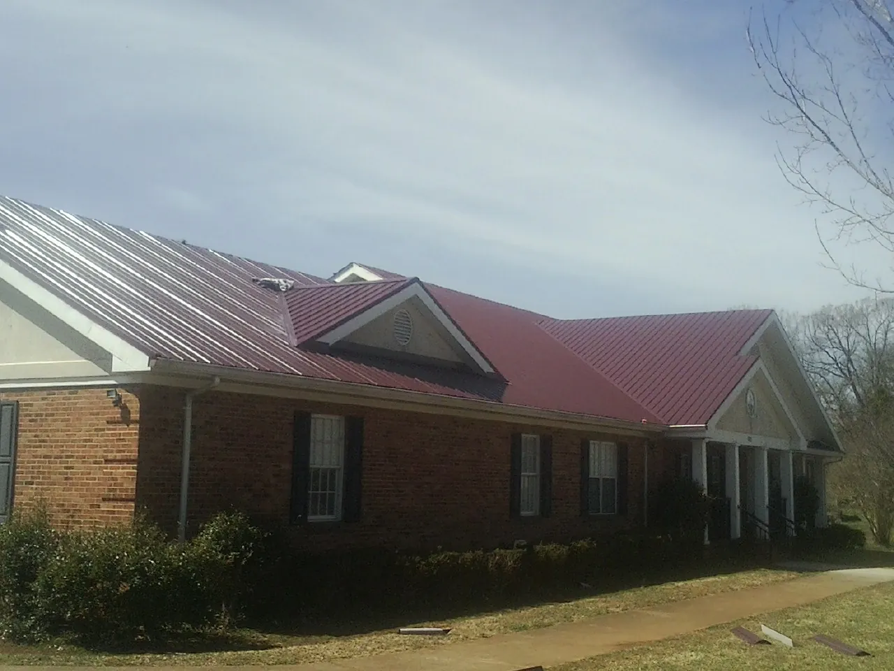 Red metal roof with gabled entries on a long brick building, from a Hail Damage Roof Repair job in Overpeck