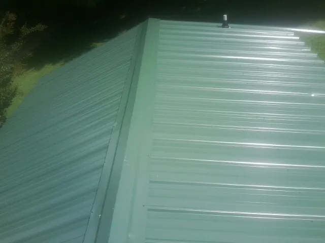 New green metal panels meeting at the ridge of a roof — Flat Roof Repair work by our crew in Overpeck