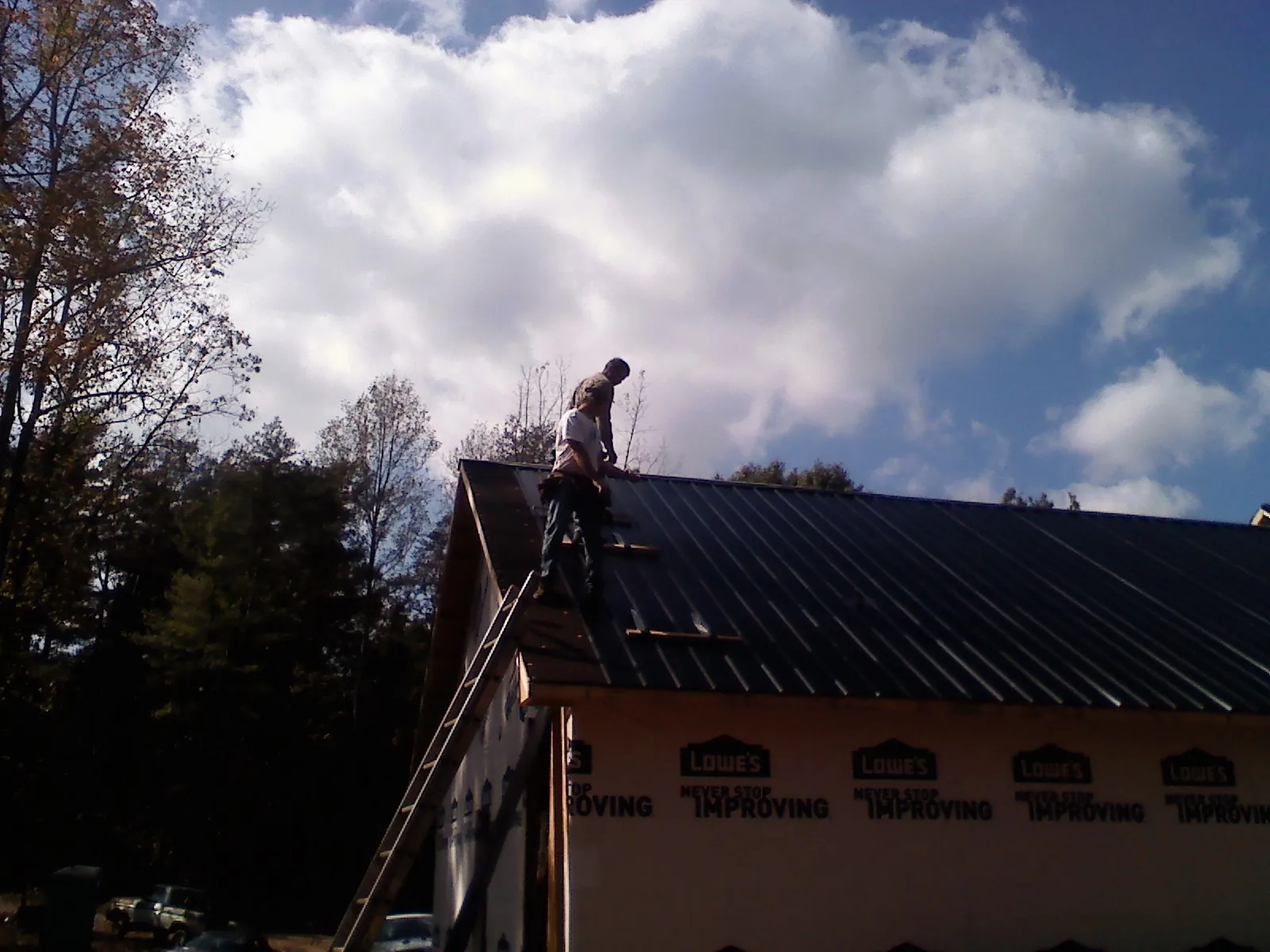 Roofer fastening dark metal panels high against a cloudy sky, from a Roof Inspection job in Overpeck