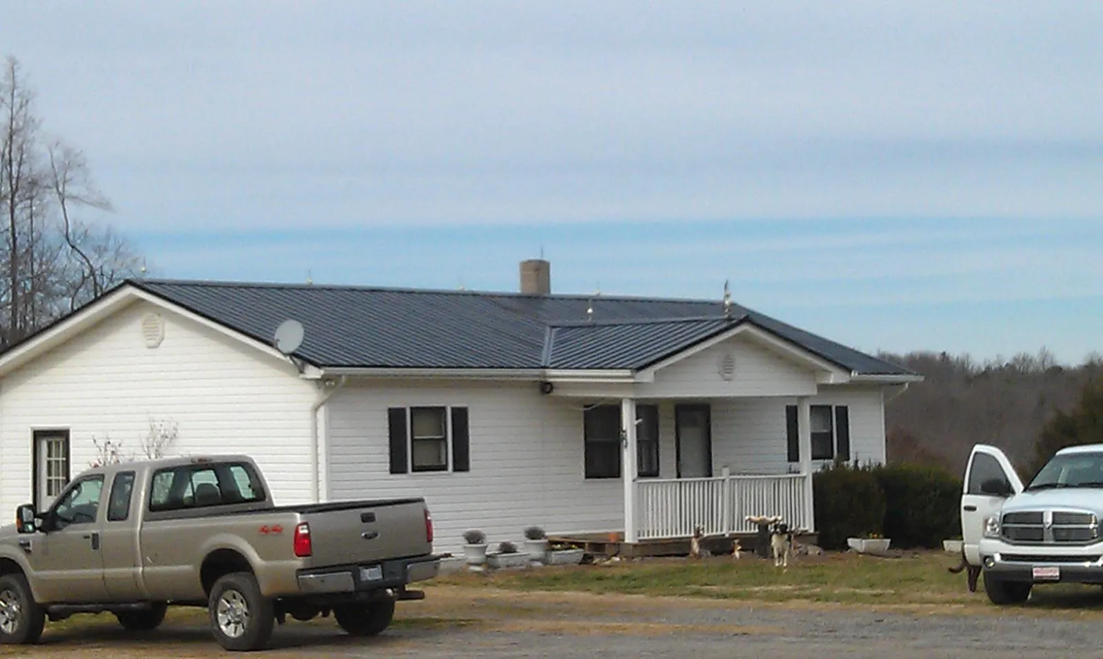 Finished dark metal roof on a white ranch home with work trucks parked in Overpeck