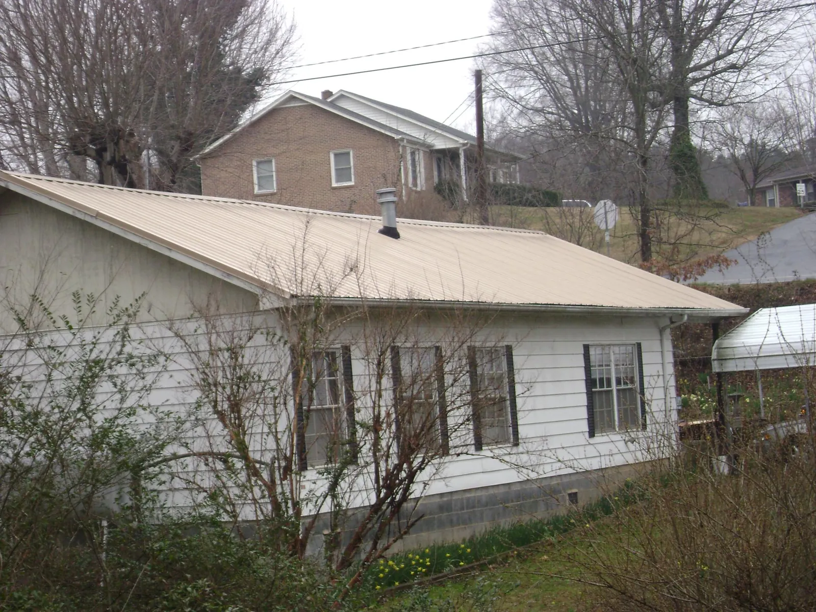 Tan metal roof on a white sided house set into a hillside — Commercial Roofing by Roofing Brothers in Overpeck
